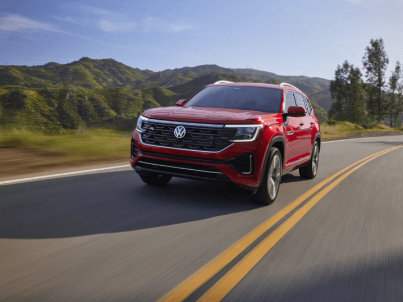 A red 2024 Volkswagen Atlas drives on a scenic hillside road.